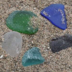 five pieces of beach glass in sand: green, cobalt, brown, aqua, and white